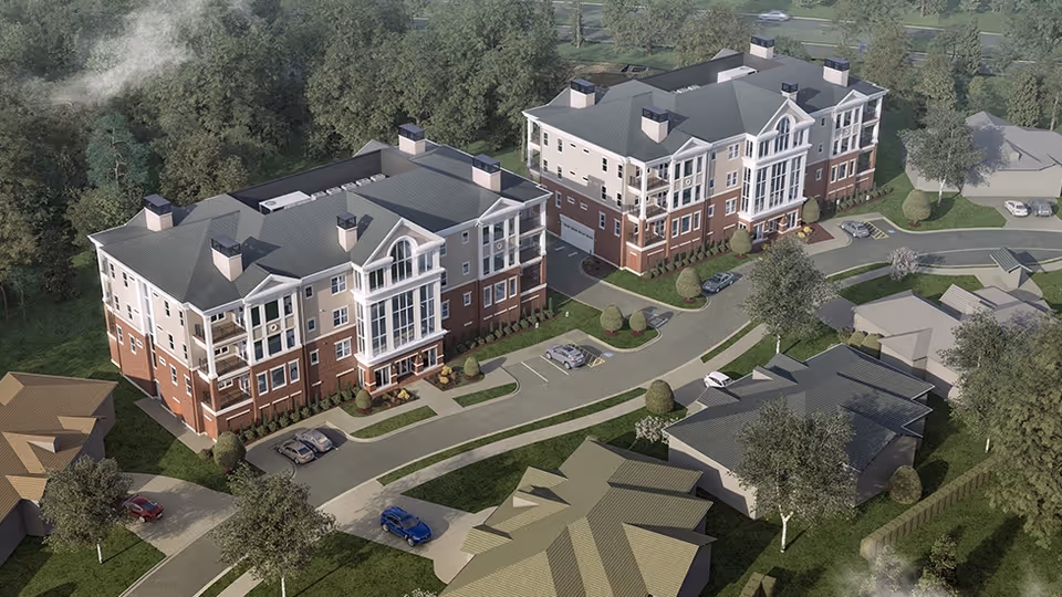Aerial view of a senior living facility named Falcons Landing featuring two large multi-story residential buildings with green roofs and brick facades, surrounded by trees, smaller houses, parking spaces, and driveways.