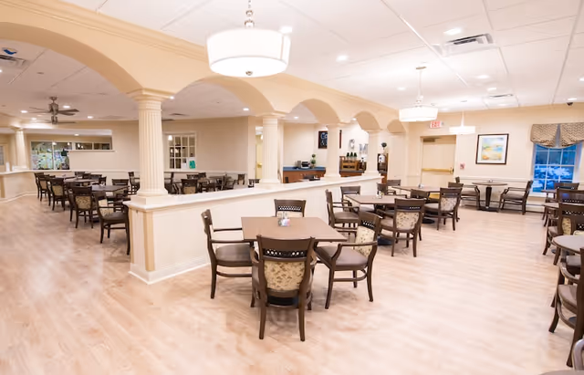 Bright, spacious communal dining room with multiple tables and chairs, arched columns, and pendant lighting.