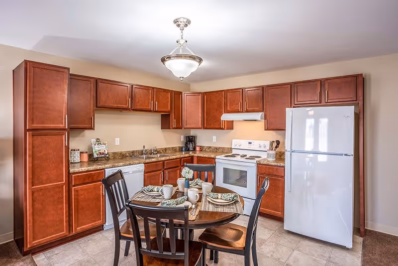 Well-lit kitchen with cherry wood cabinets, white appliances, and a round dining table set for four.
