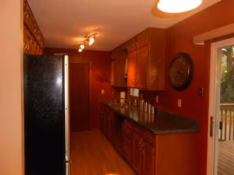 Narrow kitchen with dark countertops, wooden cabinets, and red walls.