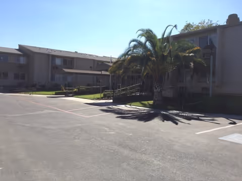Exterior view of Vintage Gardens Assisted Living Community showing parking lot and palm trees.