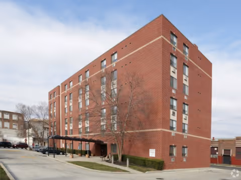 Red brick multi-story apartment building with a covered entrance and leafless trees.