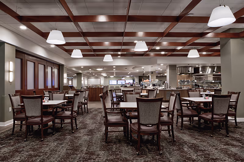 Spacious dining room with multiple tables and chairs and a food service counter under pendant lighting.