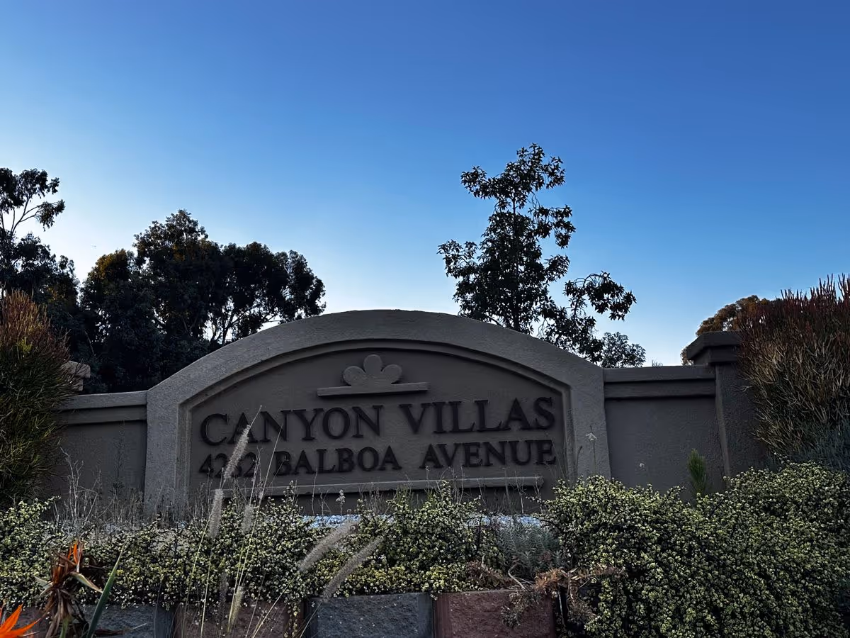Stone entrance sign reading "Canyon Villas 422 Balboa Avenue" amid landscaping with trees and a clear blue sky.