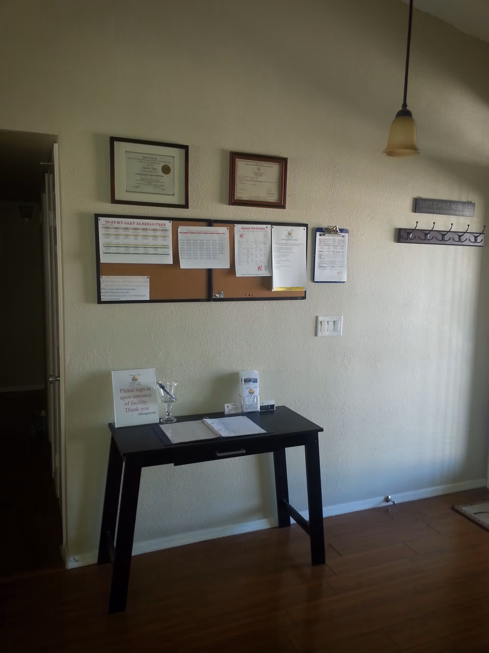 Small entry area with a black sign-in table, bulletin board with notices and framed certificates on a beige wall.