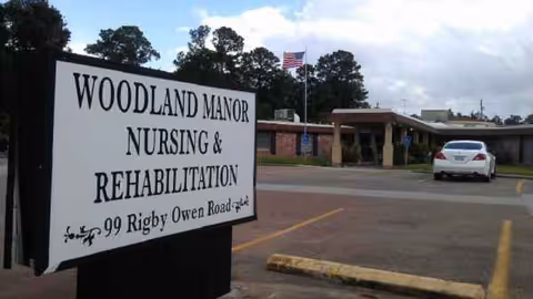 Exterior view of Woodland Manor Nursing and Rehabilitation with the entrance sign and parked car.