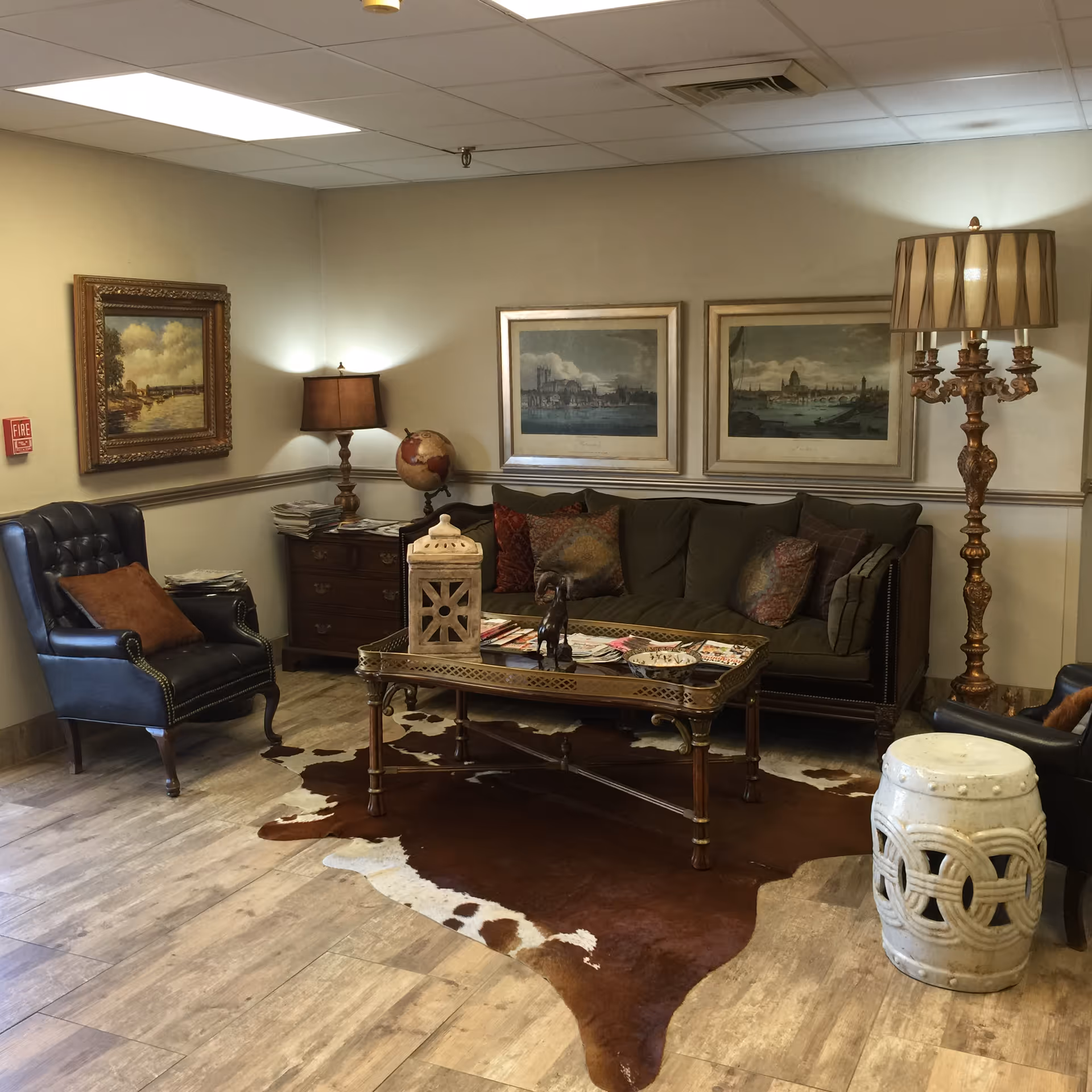 A cozy seating area with a sofa, armchairs, coffee table, lamps, framed artwork, and a cowhide rug.