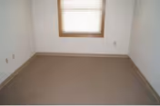 Empty small room with beige carpet, white walls, and a wooden-trim window with closed blinds.