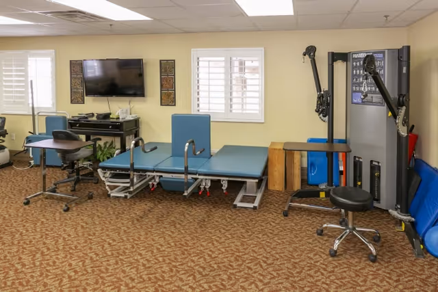 Therapy/rehab room with treatment tables, exercise equipment, a TV, and a desk.