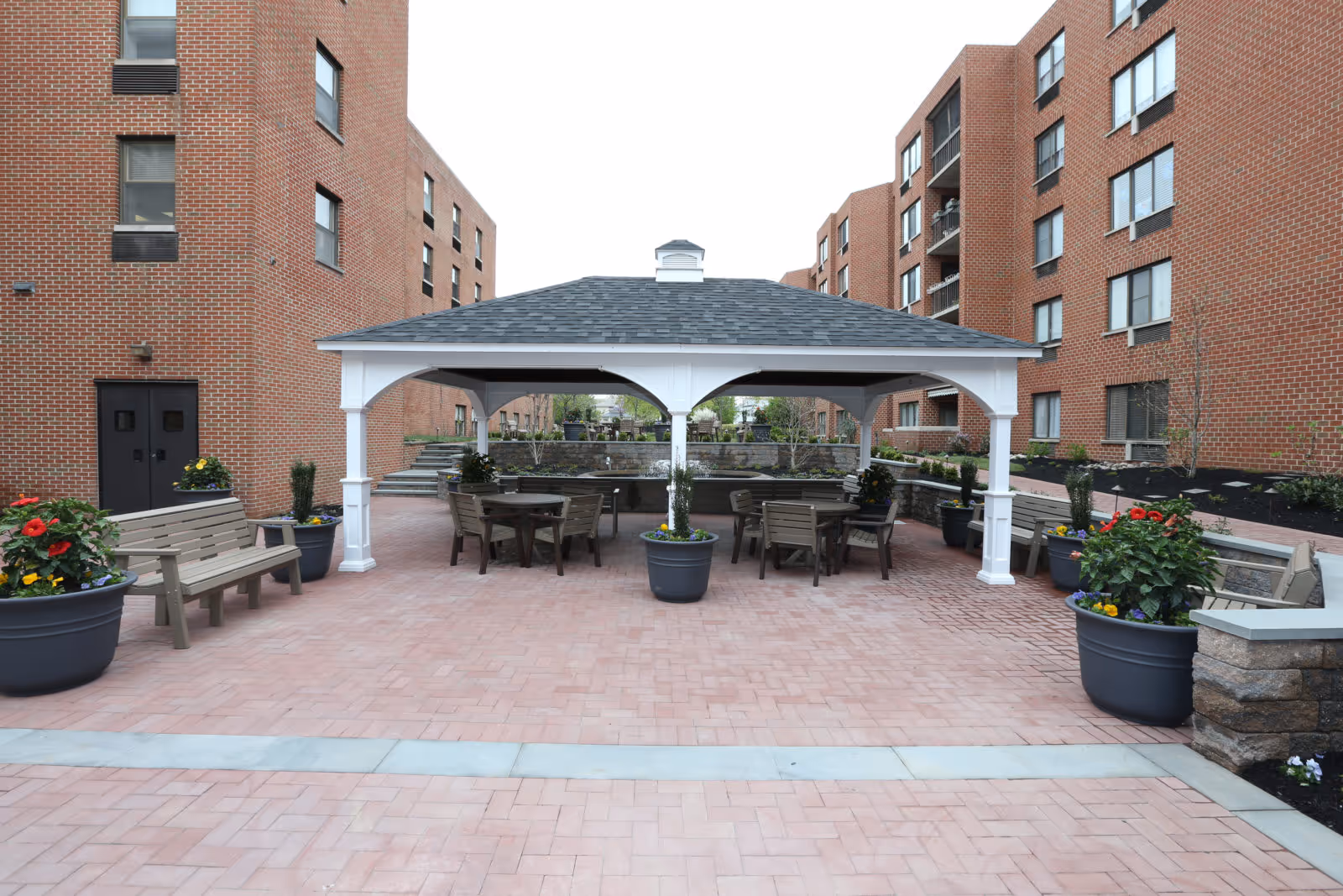 A view of a patio area featuring a gazebo with seating and potted plants, surrounded by brick buildings.