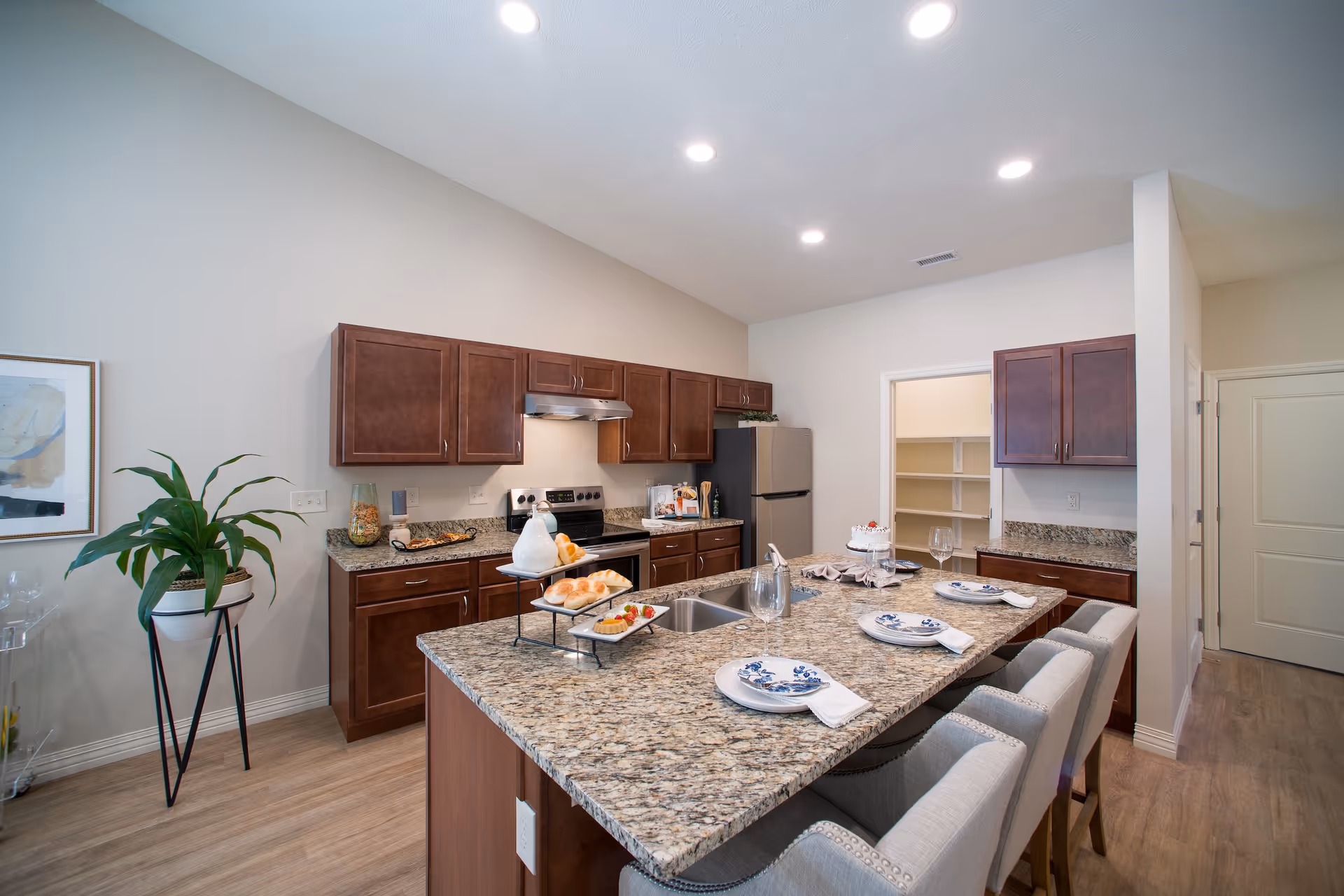Bright open kitchen featuring a large granite island with bar seating, dark wood cabinets, and stainless-steel appliances.