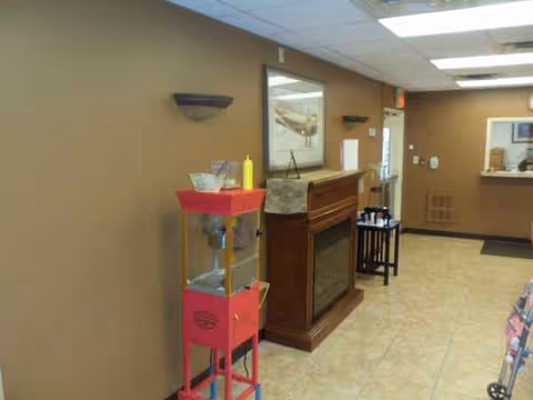 Indoor lobby with a fireplace, framed art, and a pink cart beside beige walls.