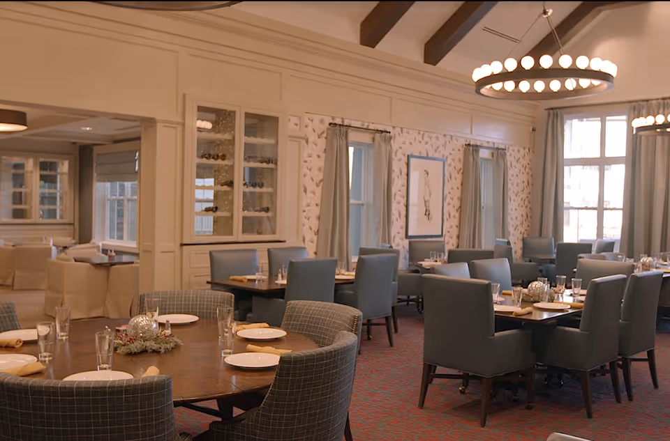 Elegant dining room with multiple set tables and upholstered chairs beneath circular chandeliers.