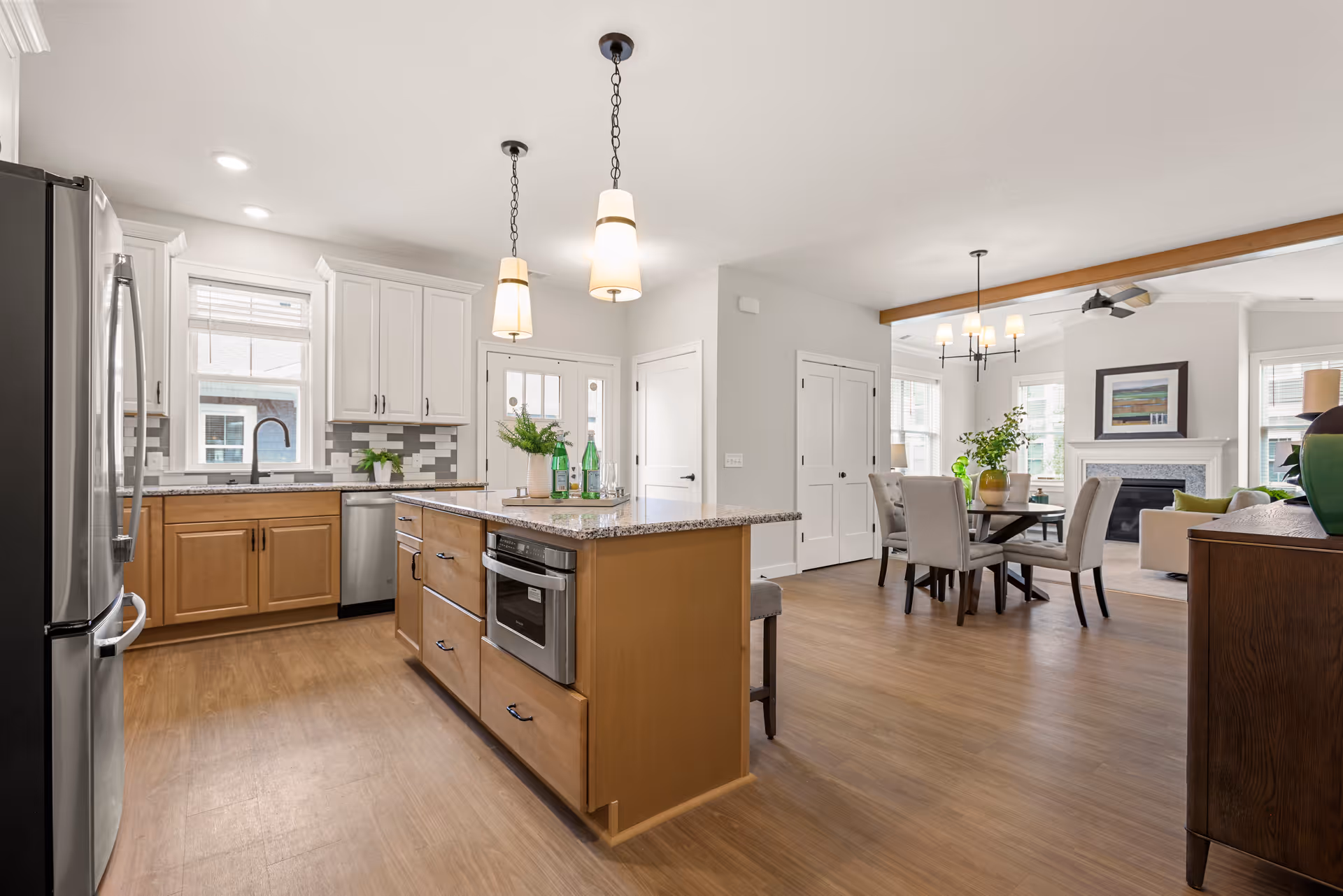 Open-concept kitchen with a central island, pendant lights, stainless steel appliances, and a dining area leading to a living room.