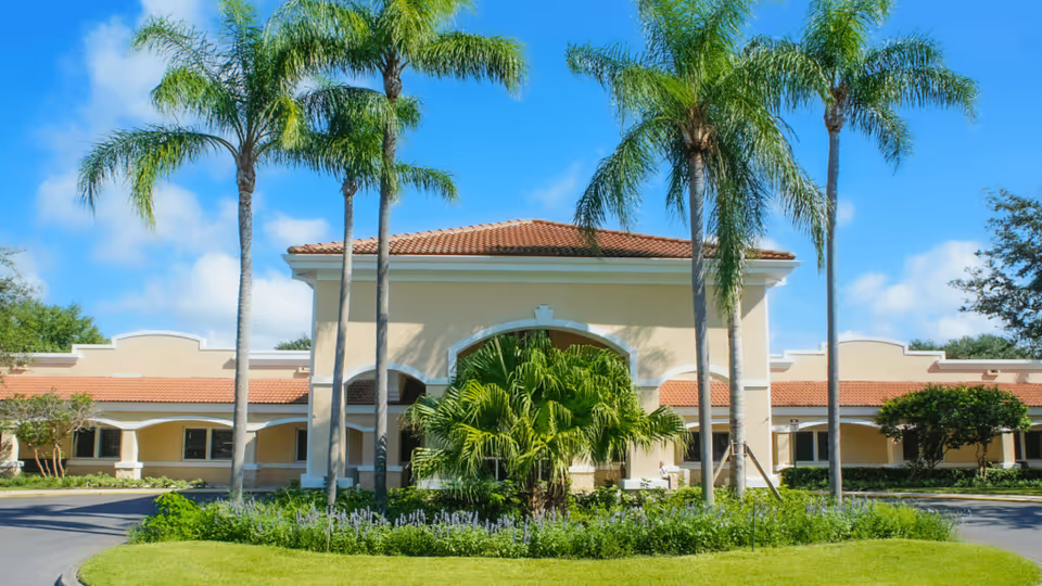 Front exterior of a single-story beige rehabilitation center with a tiled roof, palm trees, and landscaped circular driveway.