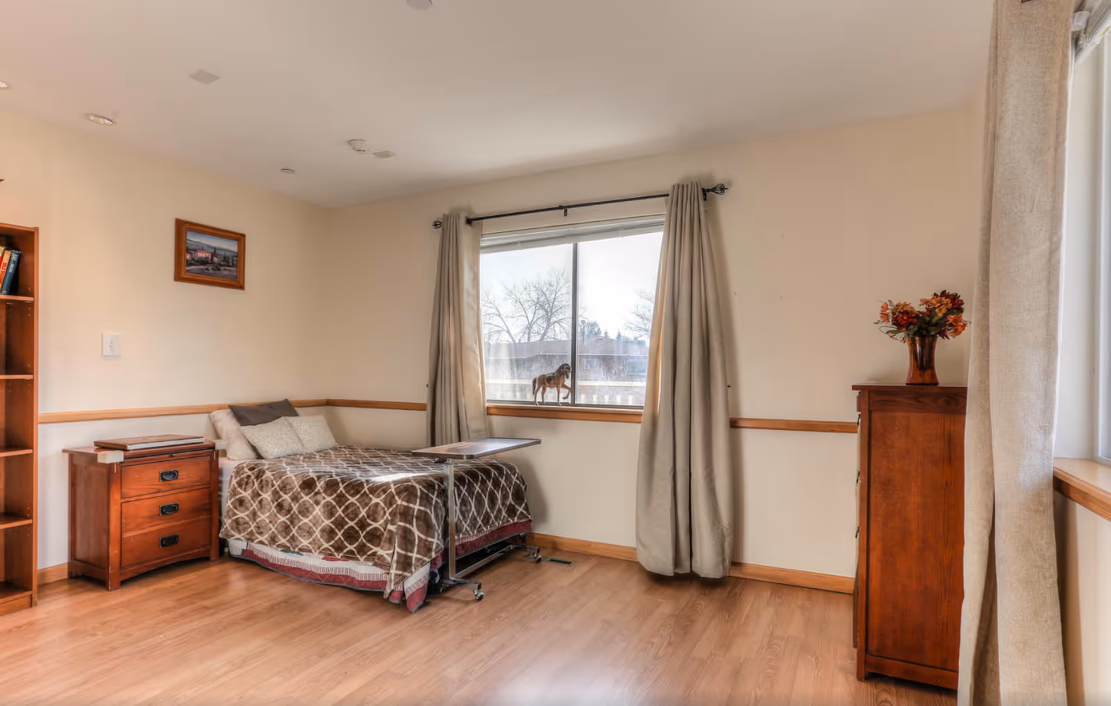 A tidy bedroom with bed, dresser, window, and neutral curtains.
