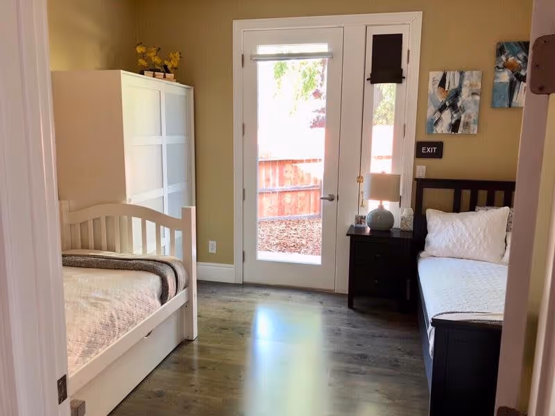Bedroom with two single beds, a nightstand and a glass door opening to a fenced yard.