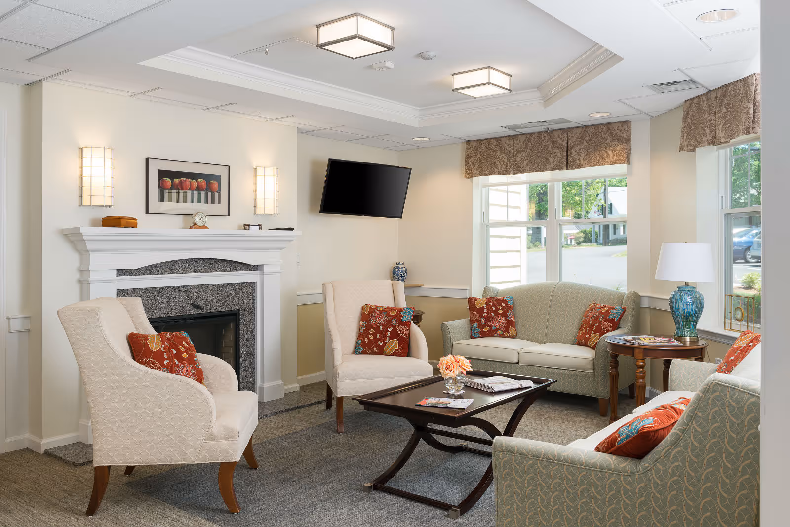 Well-lit sitting area with sofas and armchairs around a coffee table, a fireplace, wall-mounted TV, and large windows.