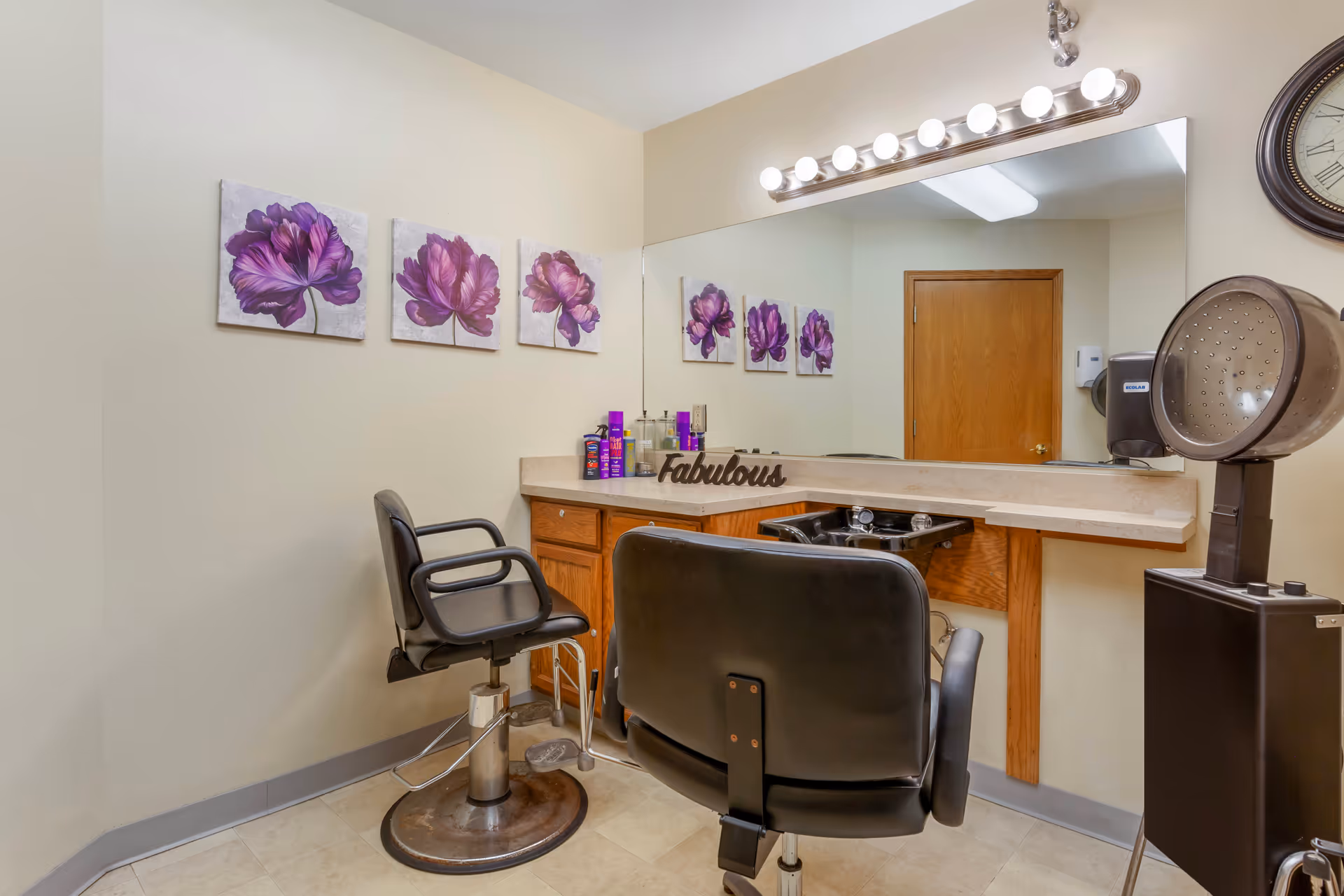 Interior salon station with two styling chairs, a large mirror, hood dryer, and purple floral wall art.