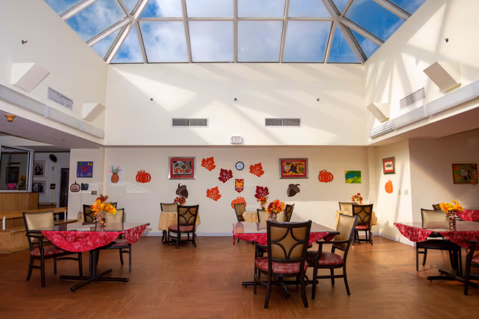 Bright dining area with tables covered in red tablecloths and decorated with autumn-themed artwork.
