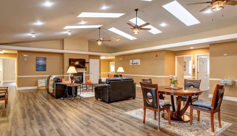Spacious senior living common area with sofas, a round dining table, and skylights.