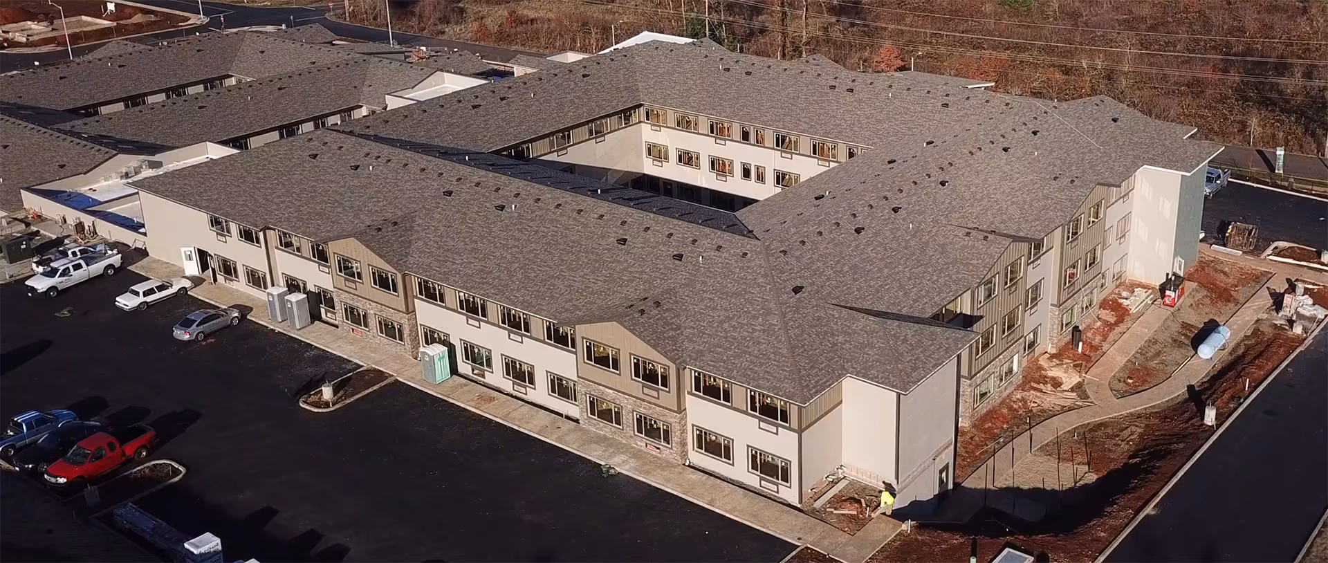 Aerial view of a large three-story senior living building arranged around a central courtyard with a parking lot and construction equipment.