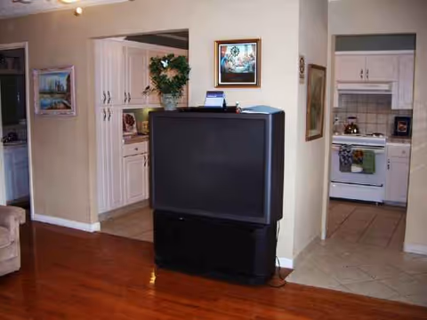 Living room with a large TV on a stand and an open kitchen beyond.