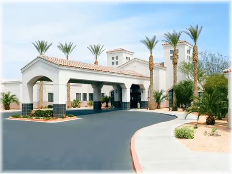 Exterior view of TLC Care Center showing a building with a covered entrance supported by columns, surrounded by palm trees and desert landscaping under a clear sky.