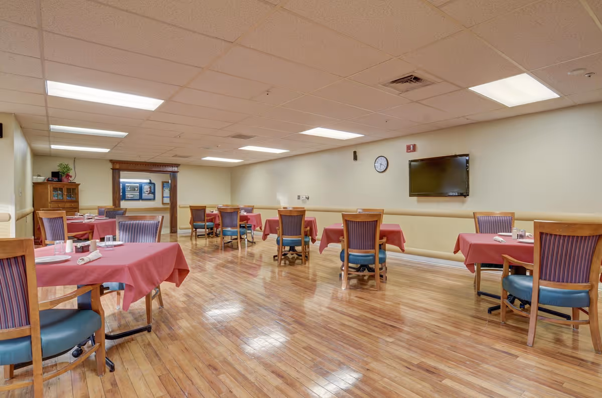 A dining area with tables set for meals in a senior living facility.