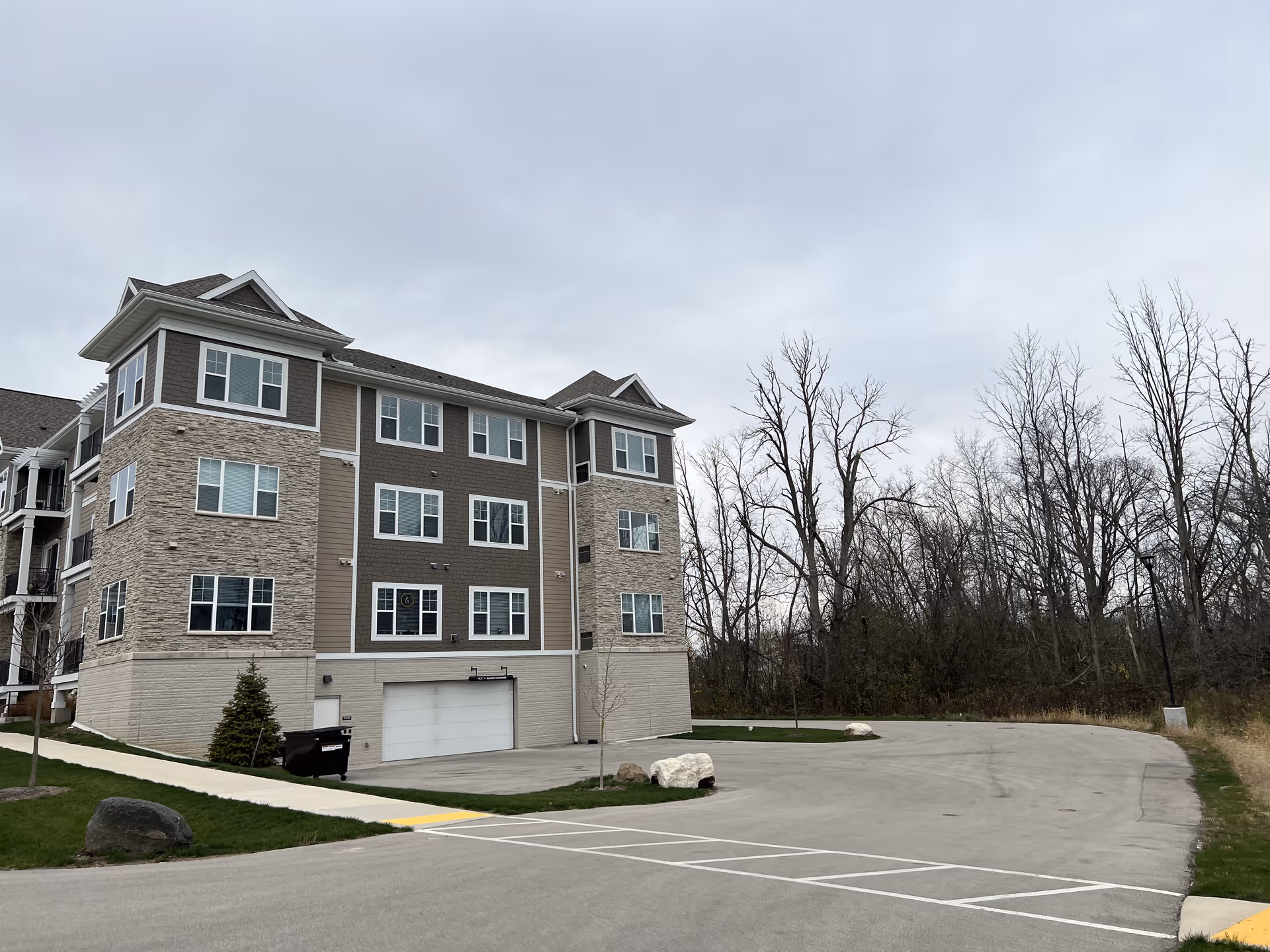 Exterior view of a multi-story senior living building with stone and siding next to a parking lot and leafless trees.