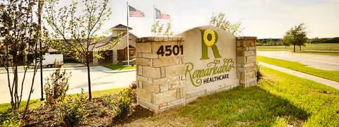 Stone entrance sign for Remarkable Healthcare of Prestonwood with flags and landscaped grounds.