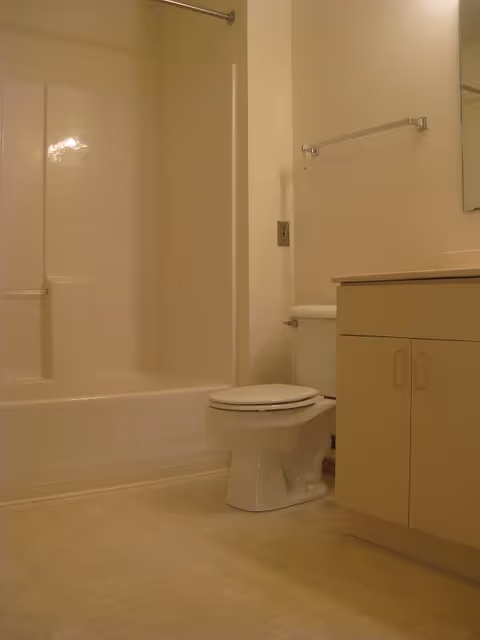 A clean bathroom featuring a white bathtub with a shower curtain rod, a white toilet, a beige vanity cabinet with a countertop, and a towel rack mounted on the wall.