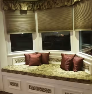 Inside a cozy window-seat nook with burgundy cushions and blinds along three windows.