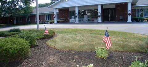 Front view of a brick senior living facility with a covered entrance and flags.