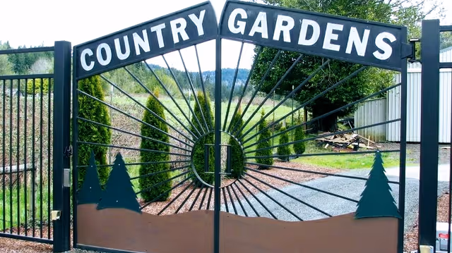Wrought-iron entrance gate reading 'COUNTRY GARDENS' with a sunburst design and landscaping beyond.