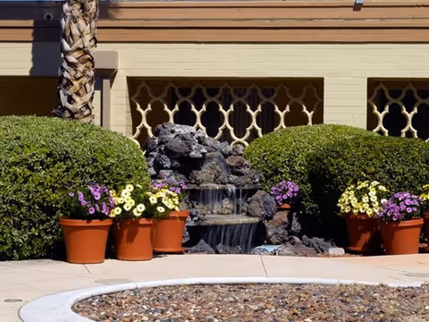 Exterior view of the facility with a rock fountain, potted flowers, and trimmed bushes.