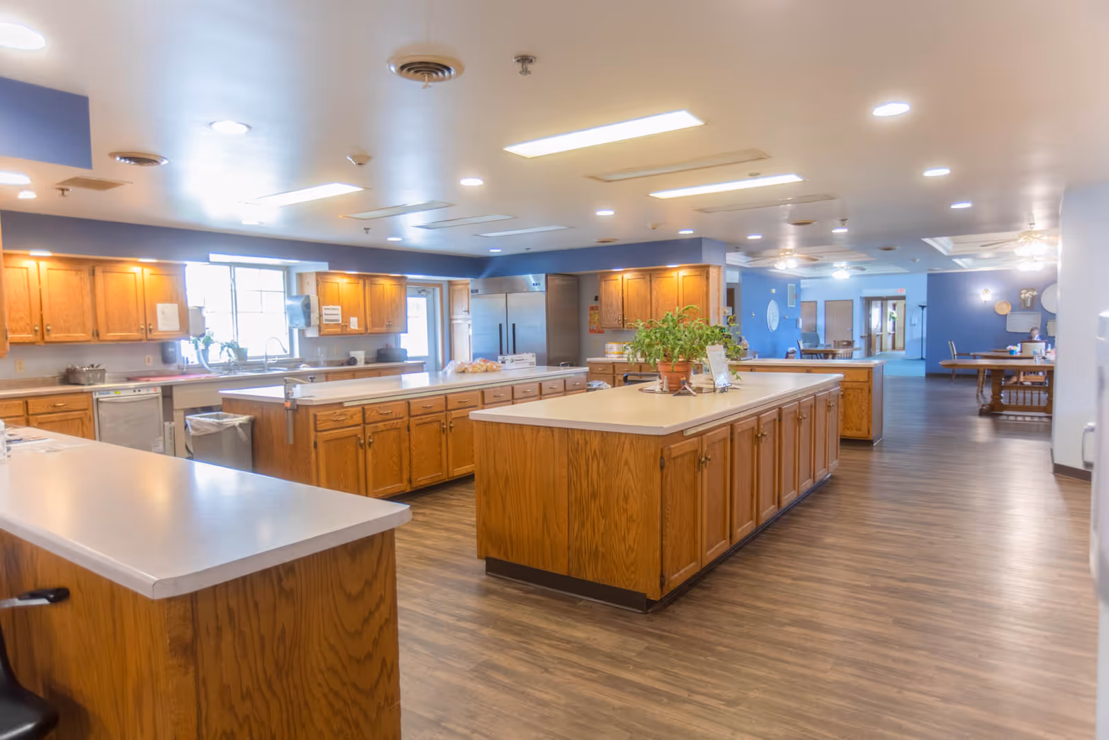 Spacious communal kitchen with multiple wooden islands, cabinets, and seating in a senior living facility.