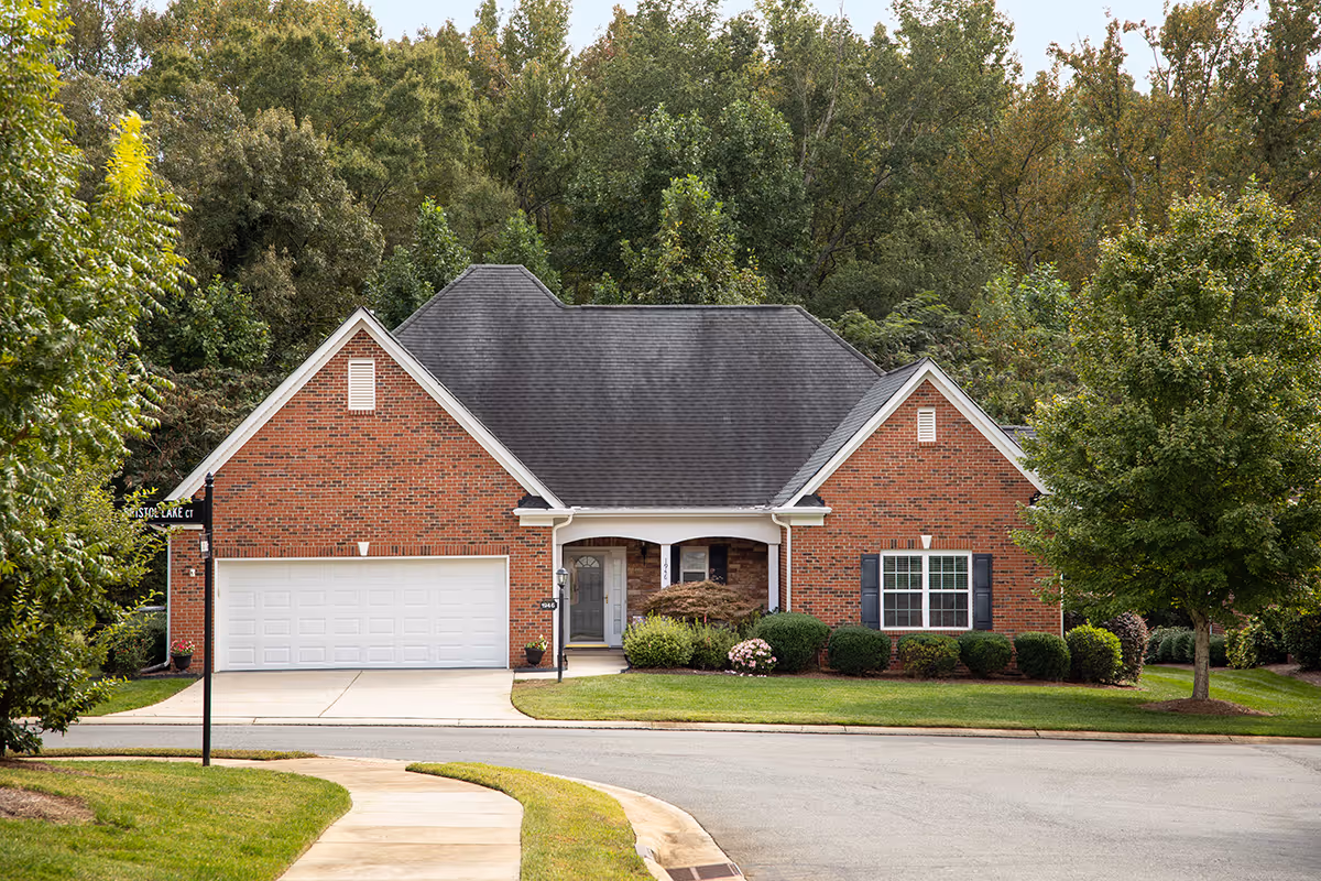 Front view of a brick suburban house with a two-car garage, manicured lawn, and trees in the background.