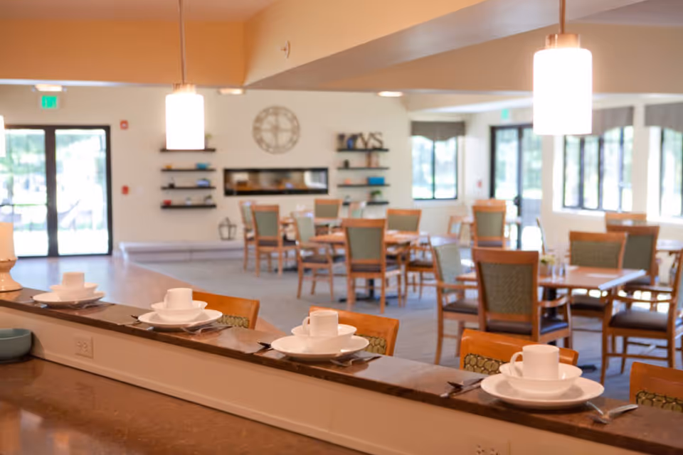 Dining room interior with a counter lined with place settings and multiple dining tables and chairs in the background.