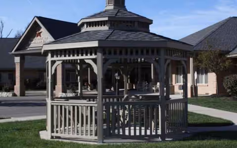 Wood gazebo on a grassy lawn in front of a senior living facility.