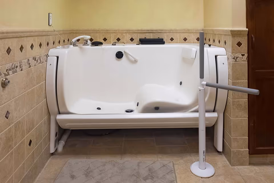 Accessible walk-in bathtub with tiled walls and a freestanding grab bar in a bathroom.