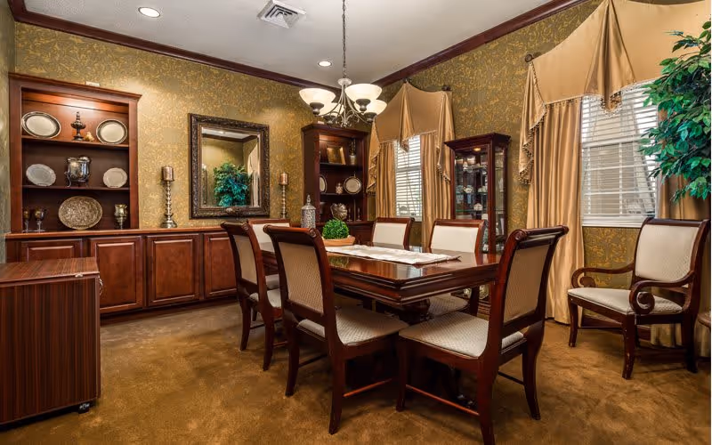 Formal dining room with a wooden table surrounded by upholstered chairs, built-in display cabinets, chandelier, and draped windows.