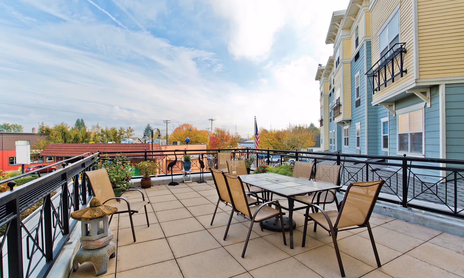 Outdoor rooftop patio with a table and six chairs, potted plants, and a view of nearby buildings.