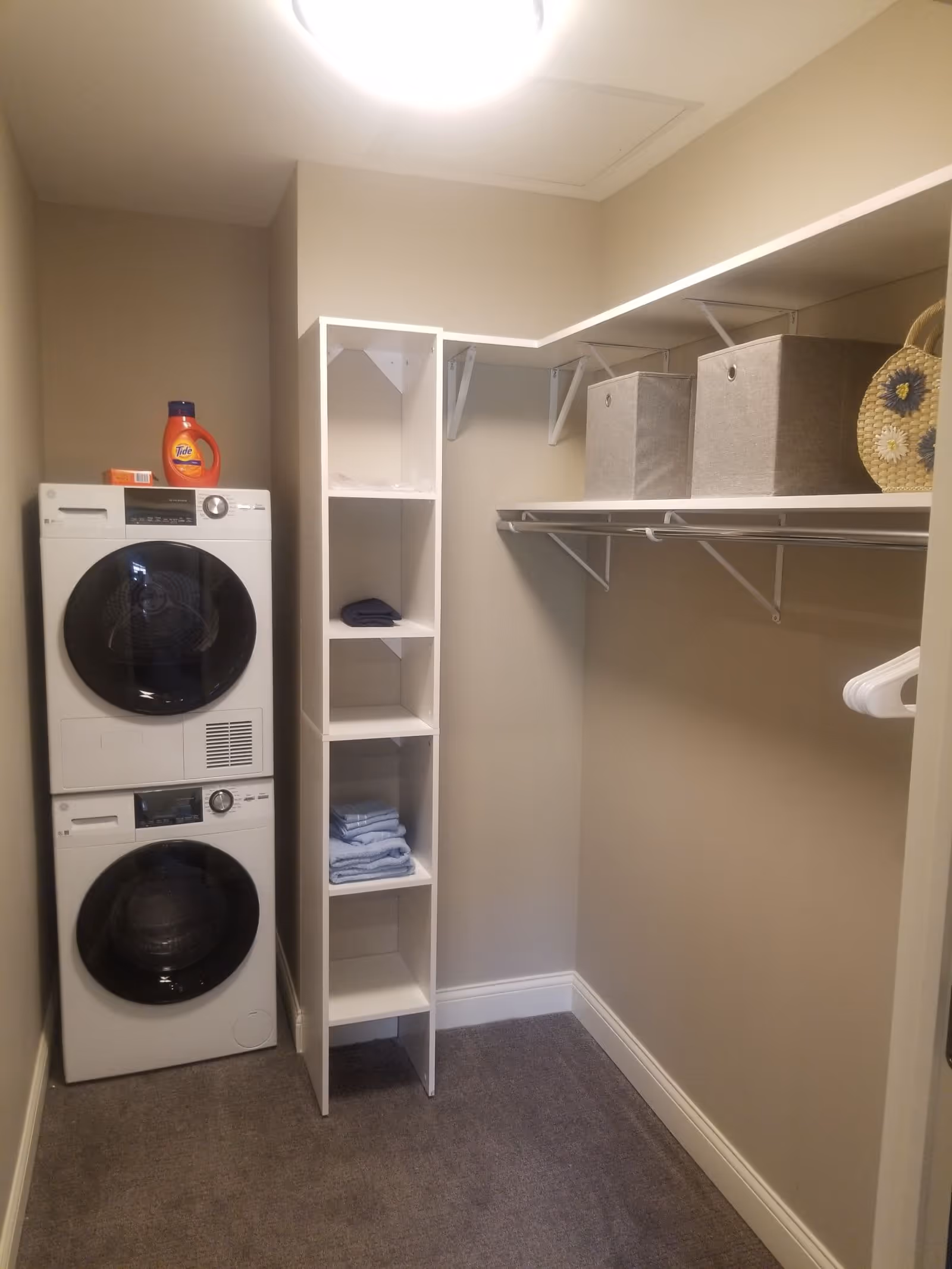 Small walk-in closet with a stacked washer and dryer, open shelving, hanging rod, and storage bins.