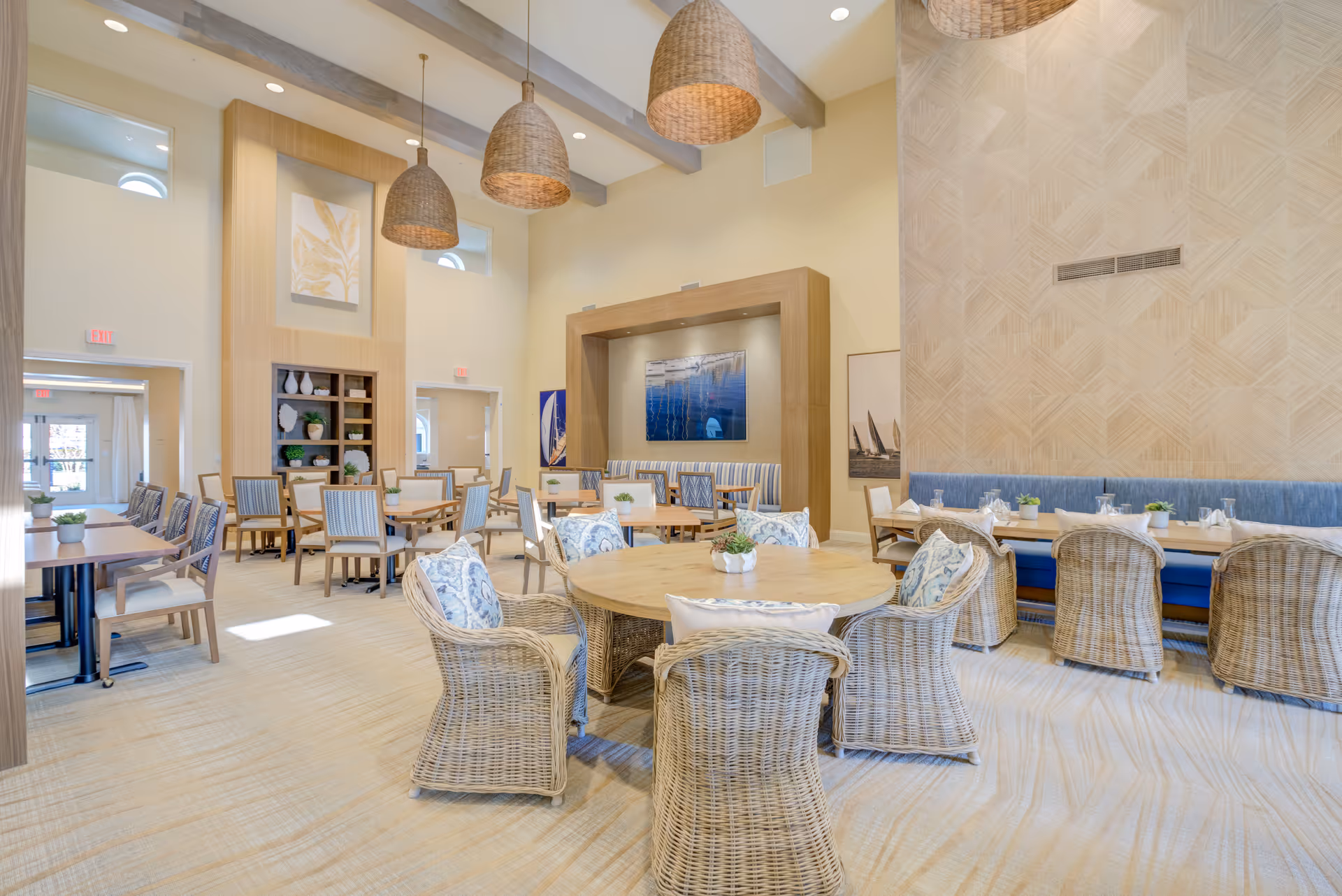 Bright, spacious dining room with wicker chairs, round and rectangular tables, pendant lights, and banquette seating.