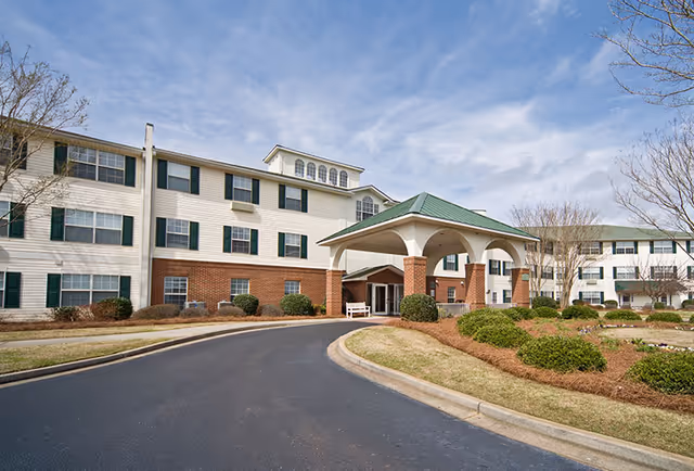Front entrance of a three-story senior living building with a covered porte-cochere, brick and light-colored siding, and a circular driveway.