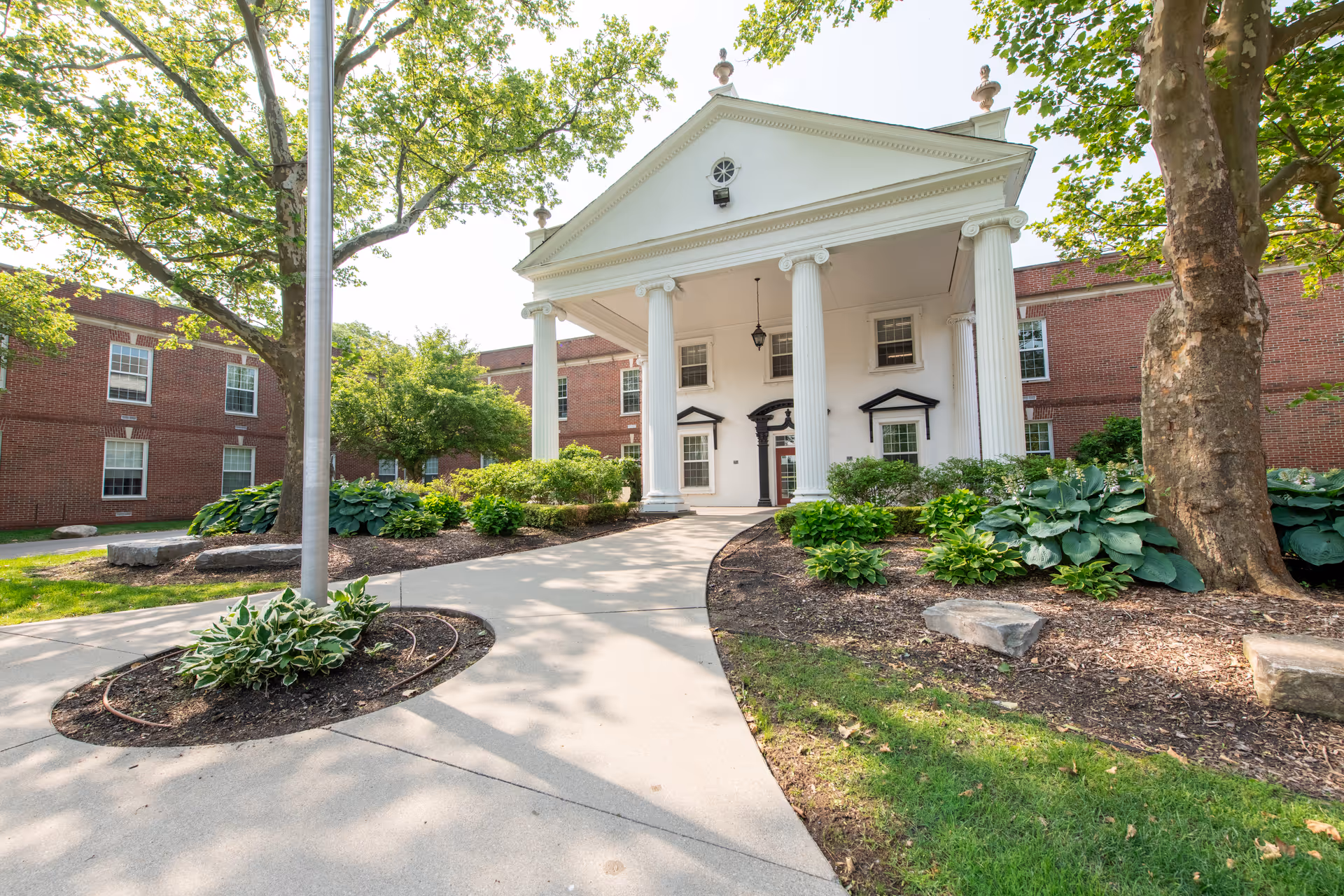 Brick senior living building with a white columned portico entrance and a landscaped walkway.