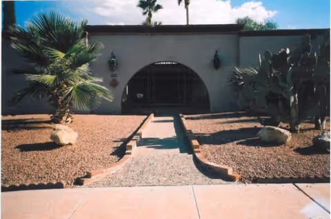 Front exterior of a senior living facility with an arched entrance and desert landscaping.