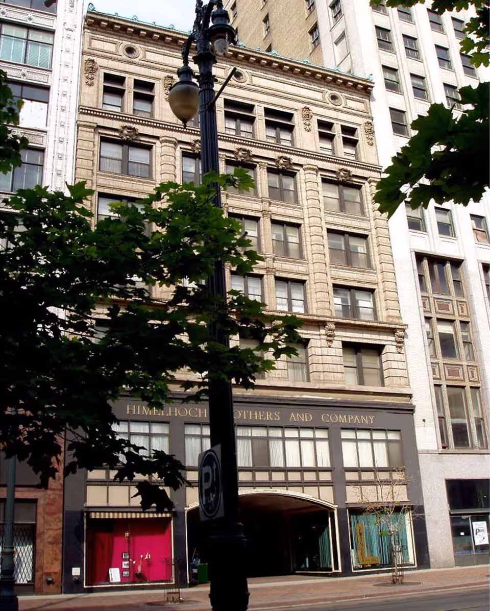Facade of a multi-story historic commercial building with a streetlamp and trees in front.