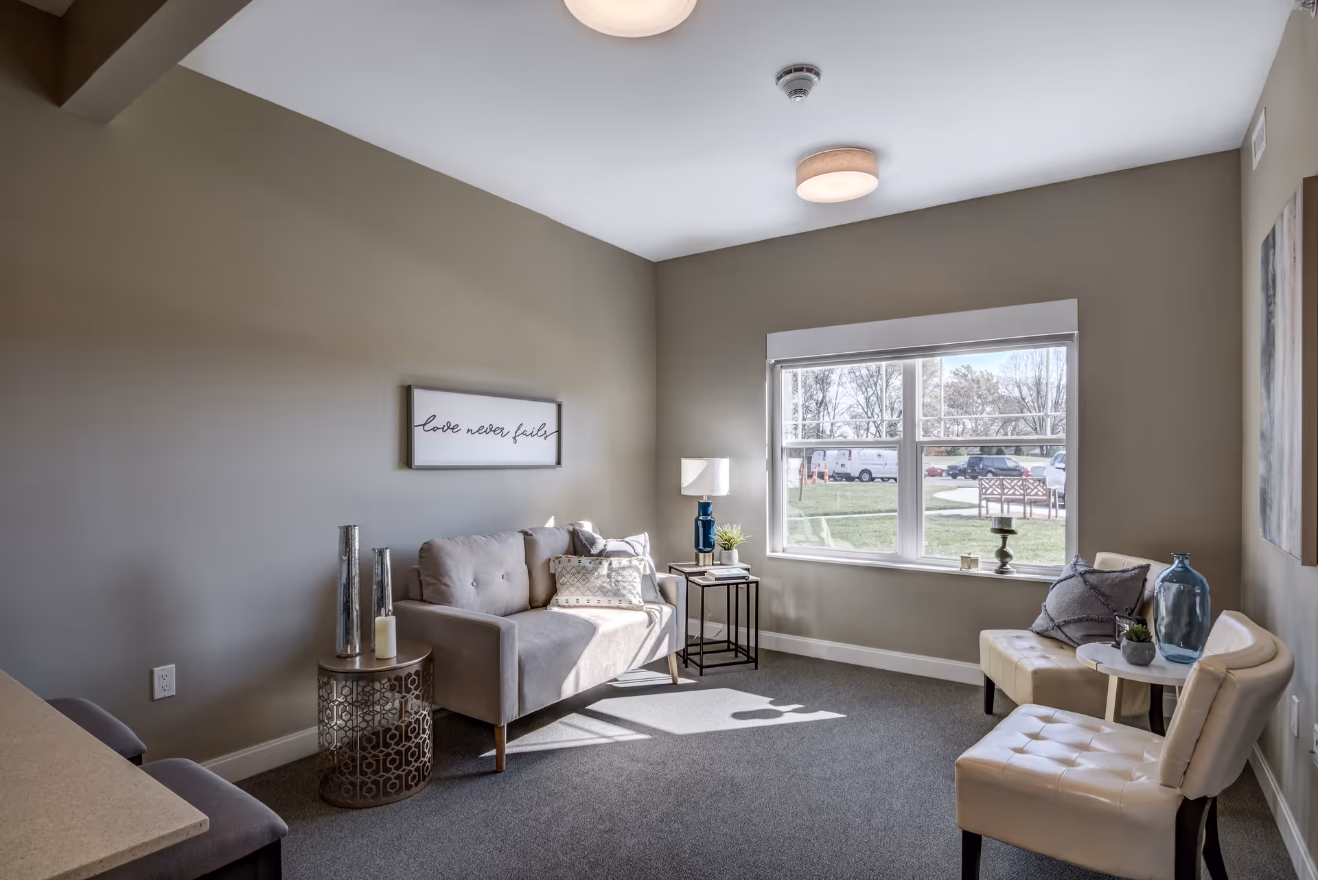 Sunlit sitting room with a sofa, armchairs, side tables and a large window overlooking the lawn.